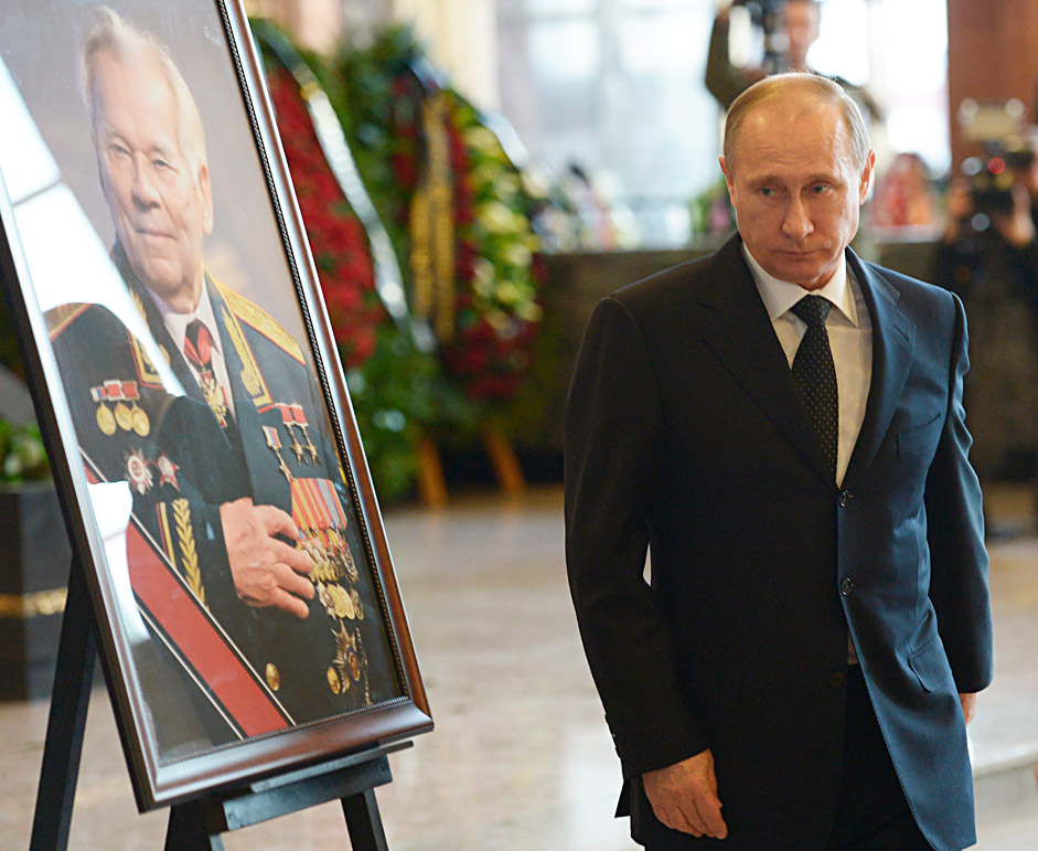 Presiden Rusia Vladimir Putin berjalan melewati sebuah potret perancang senjata api Rusia Mikhail Kalashnikov