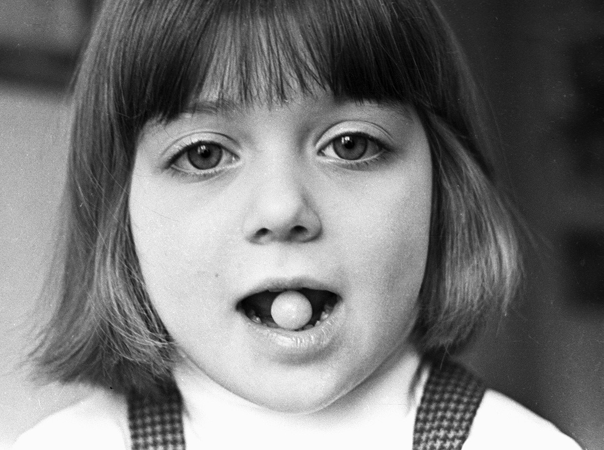 A girl holding a vaccine capsule in her teeth at the Institute of Poliomyelitis and Encephalitic Infections. 