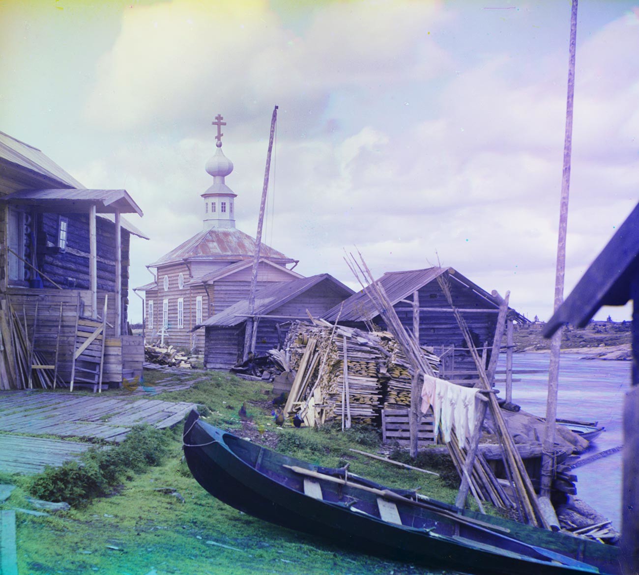 Soroka village (now Belomorsk). House overlooking Vyg River, with skiff, firewood & log sheds. Background: Church of Sts. Zosima & Savvaty. Summer 1916