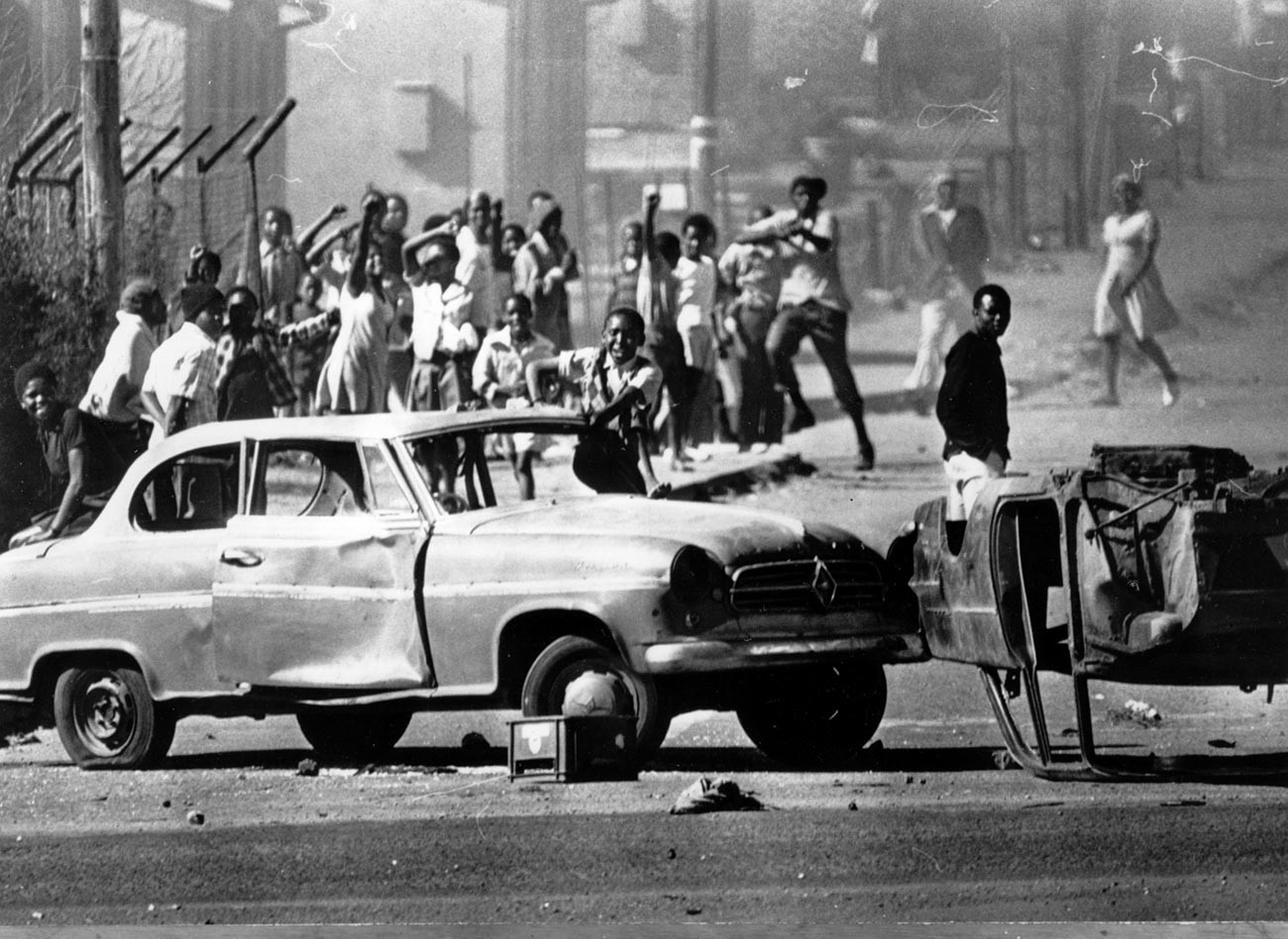 Manifestantes sul-africanos em Soweto usam carros como bloqueios durante tumultos decorrentes de protestos contra o uso de africâner nas escolas
