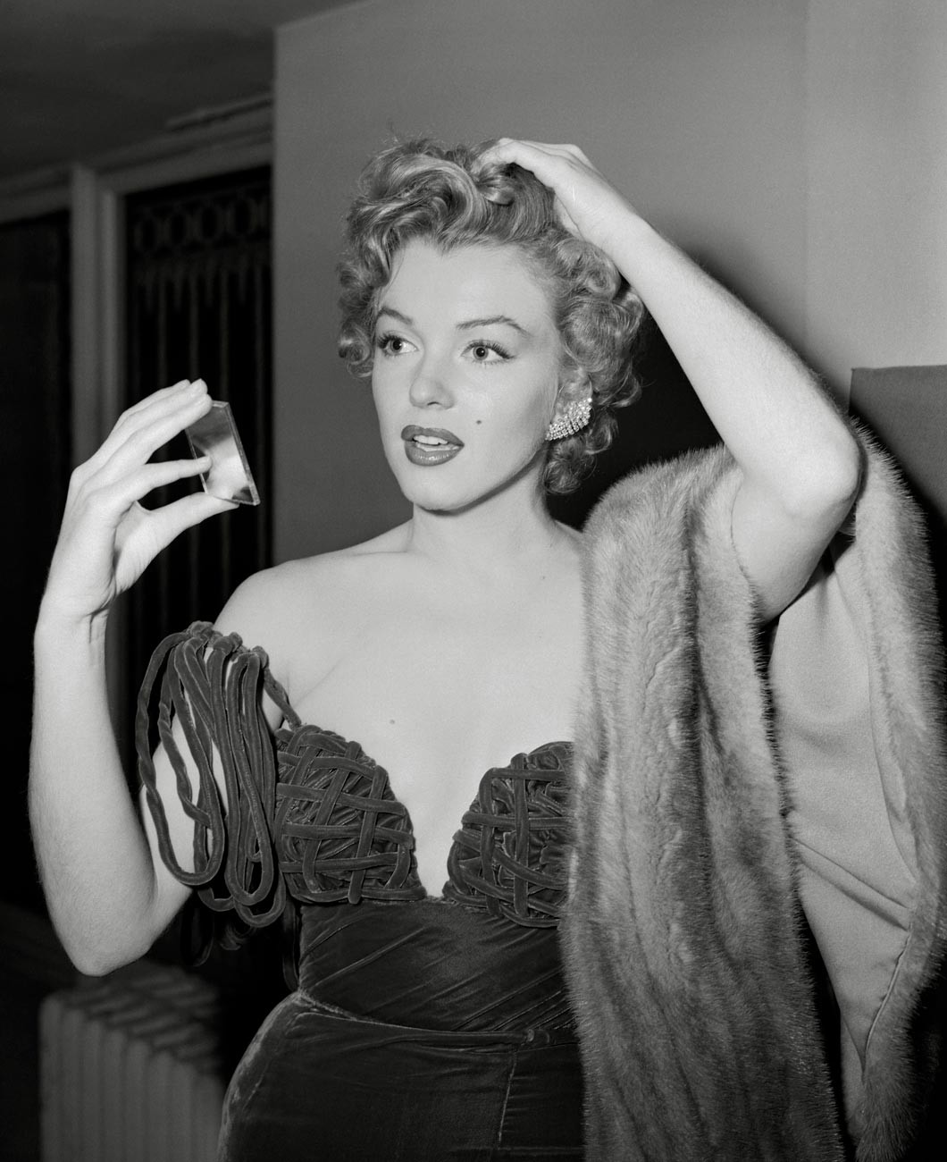 Marilyn Monroe hält sich bei den Golden Globe Awards 1952 einen Spiegel vors Gesicht und trägt ein Kleid von Oleg Cassini.