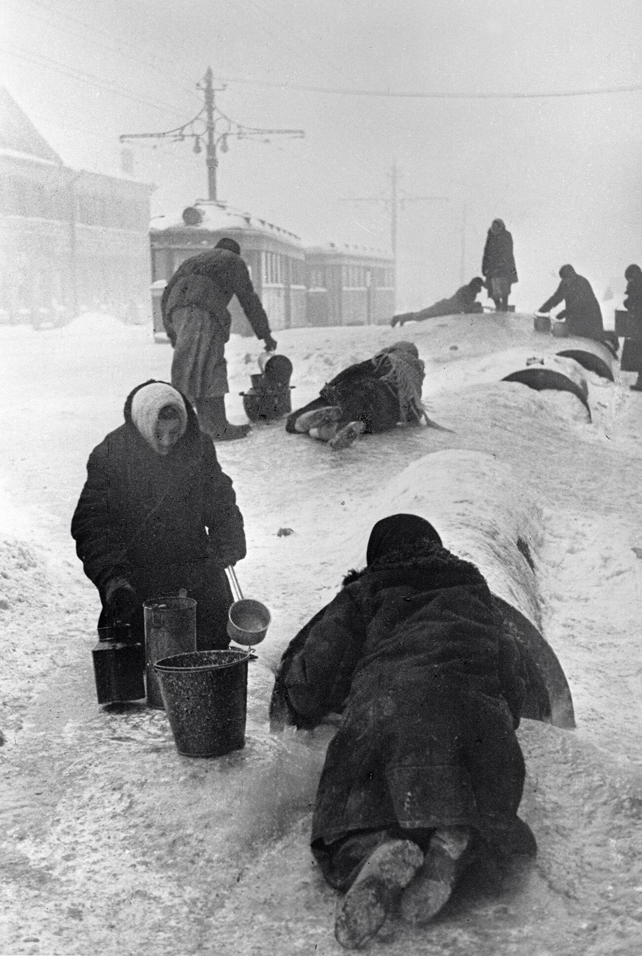 Жители блокадного Ленинграда набирают воду из разбитого водопровода на обледенелой улице.