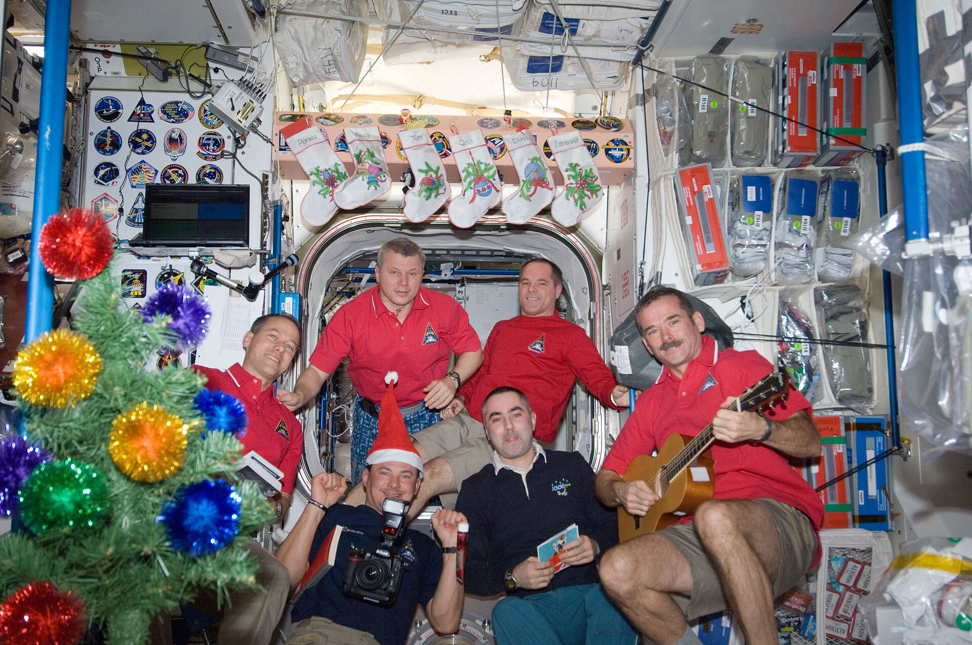 Astronauten versammeln sich im Unity-Knoten der Internationalen Raumstation für eine Weihnachtsfeier am 24. Dezember 2012. Im Uhrzeigersinn (von oben rechts) abgebildet sind der NASA-Astronaut Kevin Ford, Kommandant; Chris Hadfield, Ewgeny Tarelkin, Roman Romanenko, Tom Marshburn und Oleg Novitskiy.