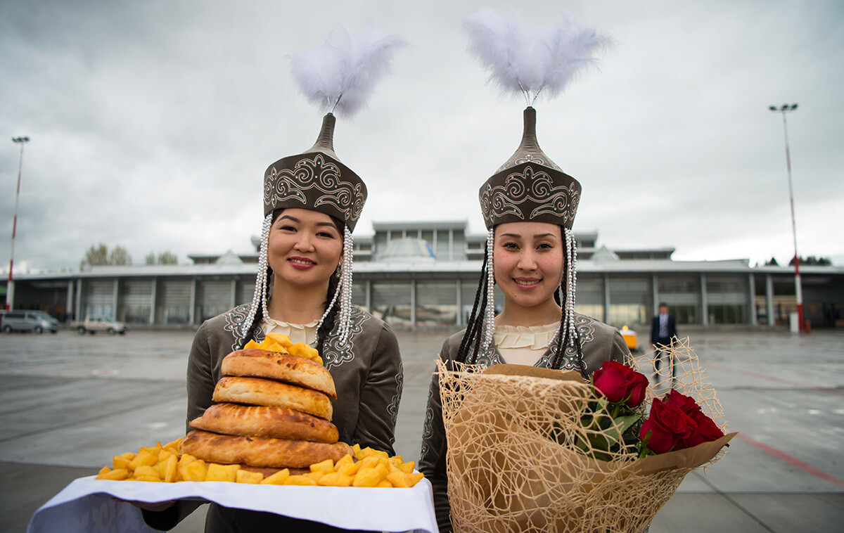 Dua perempuan muda dengan pakaian tradisional membawa bunga dan makanan untuk menyambut kedatangan turis di bandara di Bishkek, Kirgizstan.
