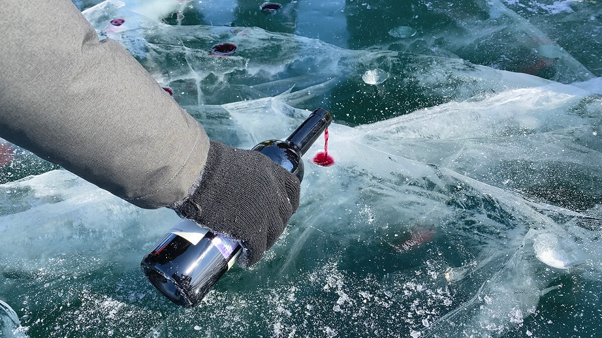 Kiss of Baikal is entertainment for tourists. A man pours wine into improvised glasses from frozen Lake Baikal