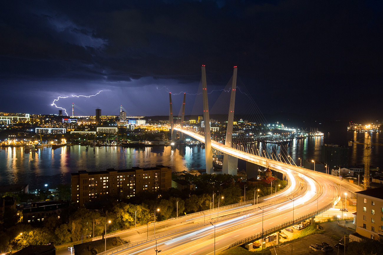Lightning strikes the city skyline at night beyond the Golden bridge on Golden Horn Bay in Vladivostok 