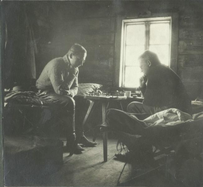 1914-1918. Deux hommes jouent aux échecs dans une maison de campagne en bois.