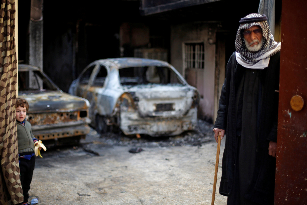 Seorang pria tua dan seorang anak berdiri di depan sebuah rumah yang dibakar oleh militan ISIS sebelum mereka melarikan diri dari daerah tersebut, di lingkungan Arabi, kota Mosul, Irak. Sumber: Reuters