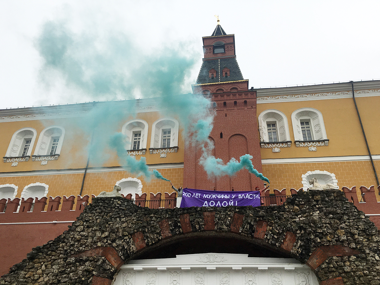 Feminist activists unfurl a banner with a message reading "Men have been in power for 200 years. Down with it!" and light smoke flares outside the Kremlin on the International Women's Day. / Photo: TASS