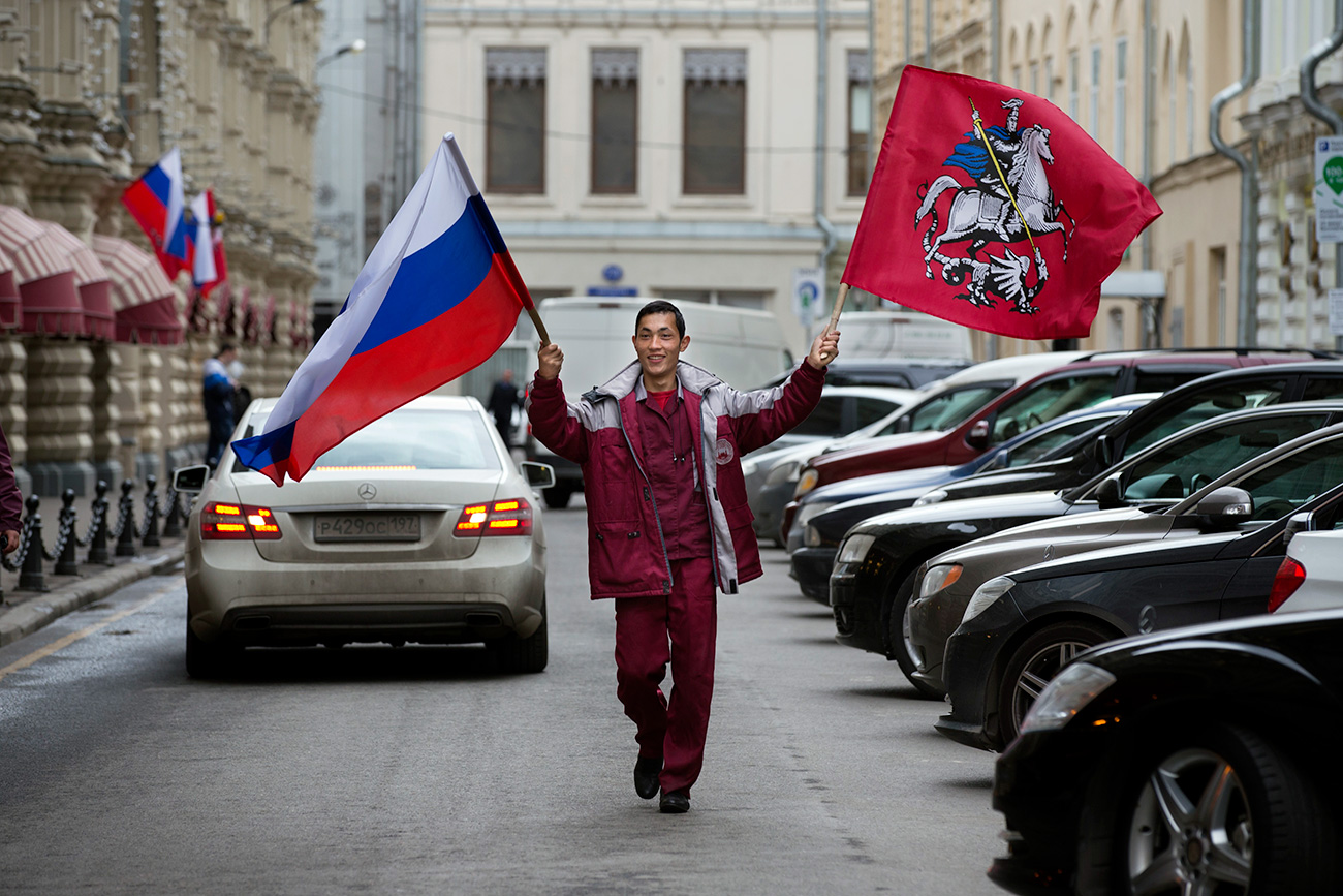 2015年4月30日、モスクワの赤広場の近くにあるデパート・グム（GUM）に飾るために、タジクの移民の労働者がロシア全土とモスクワ市の旗を持つ＝ Russia / AP