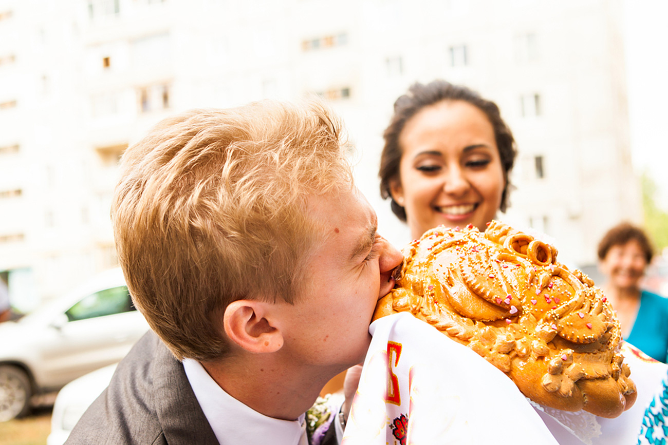 Closeup photo of bride and groom nibbling traditional loaf. / Legion Media
