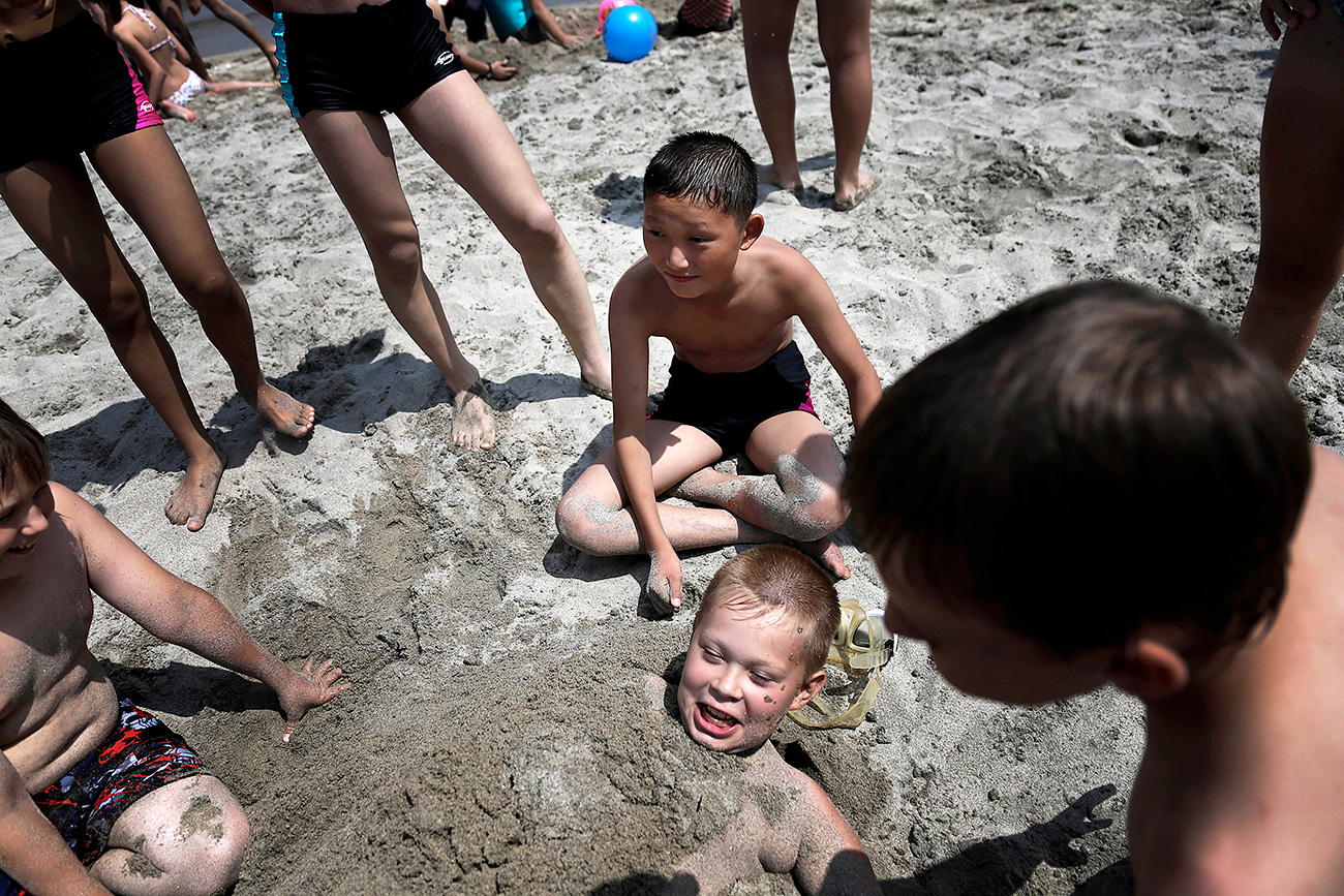 Children bury a Russian boy in the sand at the Songdowon International Children's Camp / AP