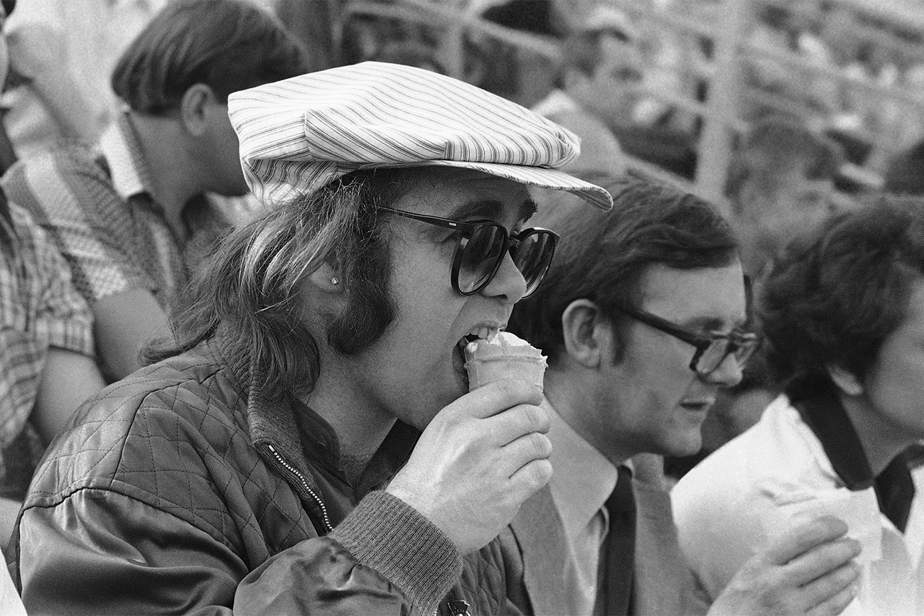 A estrela do pop Elton John comendo sorvete enquanto assistia a um jogo de futebol em Moscou entre o time do exército e o Dinamo de Minsk, em maio de 1979. / Foto: AP