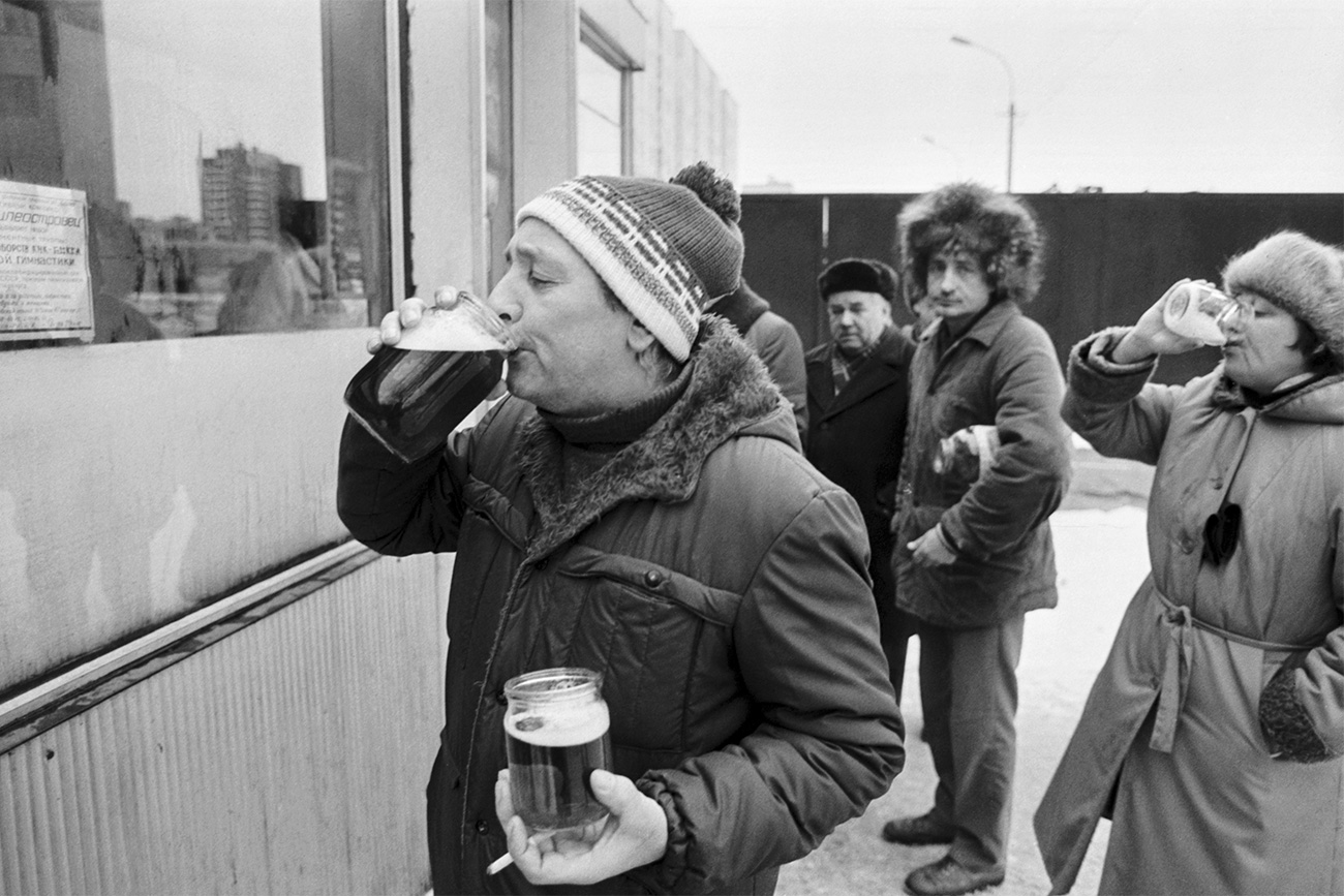 Un uomo beve birra davanti a un chiosco dopo aver riempito due barattoli. Fonte: Nikolaj Adamovich/TASS