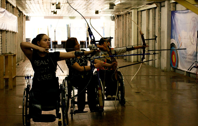 Disabled wheelchair-bound Natalia Ryzhova (h), Svetlana Barantseva (c) and Margarita Sidorenko attend a training session of a local amateur archery club on the suburbs of Russia's Siberian city of Krasnoyarsk, May 3, 2012. Disabled people have the possibility of learning the sport of archery for free due to financial support from the newly created state regional centre of adaptive sport, according to club members. The banner reads "Hello to participants of competitions".  Reuters/Vostock-Photo